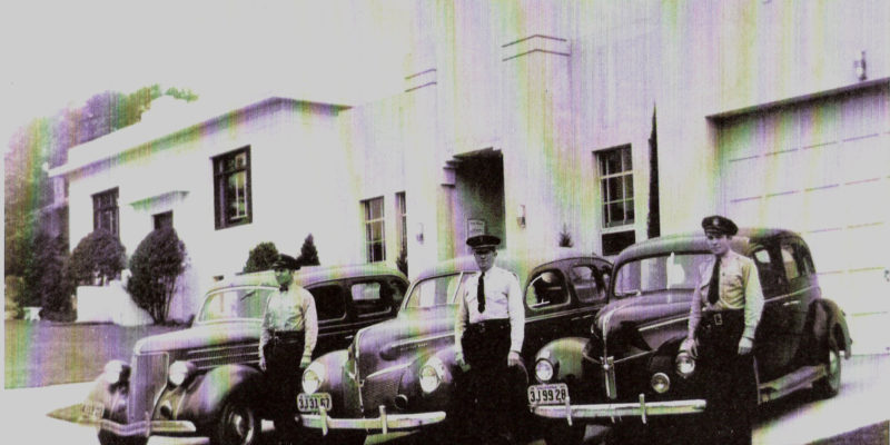 Group photo of Sebastopol Police Department, taken sometime between January 2, 1940 and August 2, 1941. Cars are parked in front of the City Hall and Police Department on Bodega Avenue. Left to right: Jim Morris, Chief Ed Foster and Bill Lawrence. Officers used their own vehicles and mounted red lights on front. L to R: Jim Morris, Chief Ed Foster, Bill Lawrence.